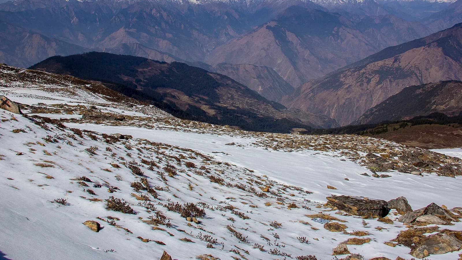 A snow-covered mountain path leading toward layered Himalayan ridges under a clear sky
