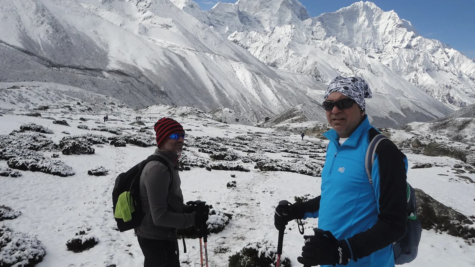 Trekkers walking down a stony Khumbu trail with snow-capped Himalayan peaks behind them on the way back from Everest Base Camp