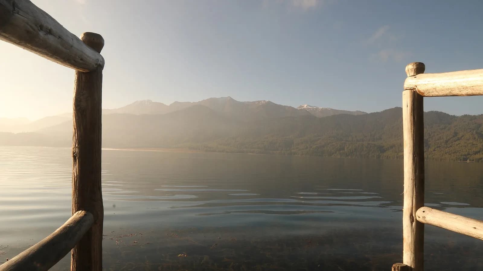 The clear blue water of Rara Lake reflecting forested hills and snow peaks in remote north-west Nepal