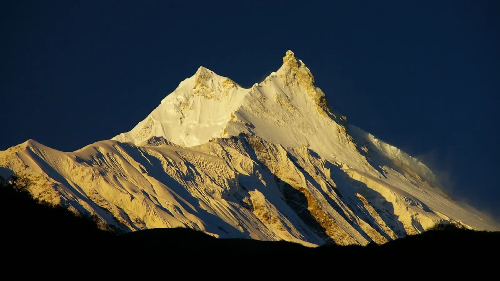 Mount Manaslu lit by sunrise, its corniced summit ridge rising above the surrounding Himalayan peaks