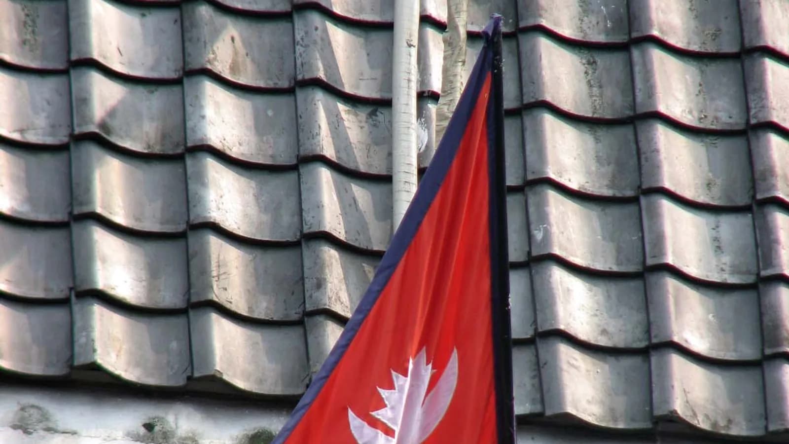 The crimson and blue double-pennant flag of Nepal flying from a pole against the sky