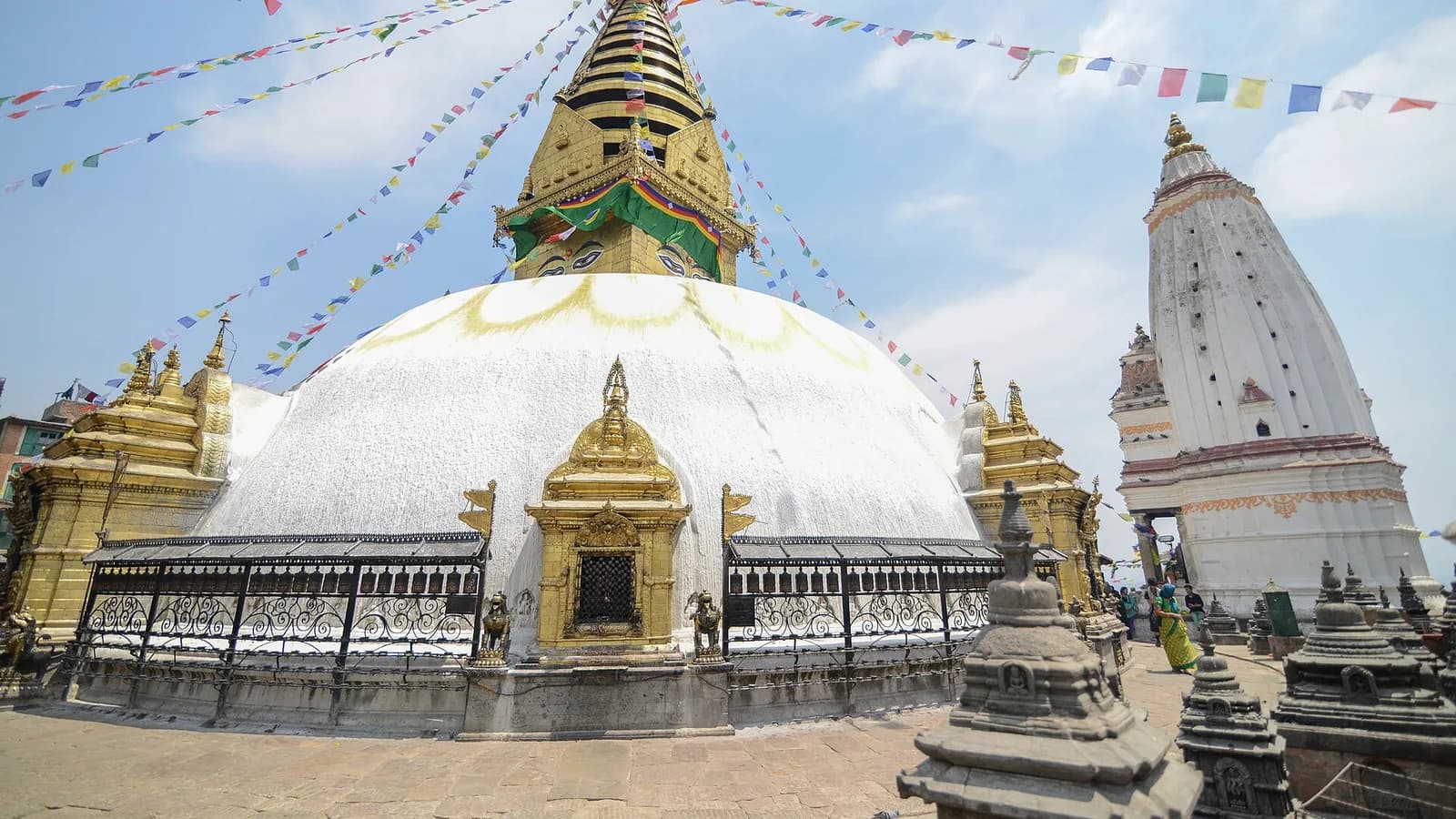 The white dome and gilded spire of Swayambhunath stupa in Kathmandu, painted with the Buddha's eyes, against a clear sky