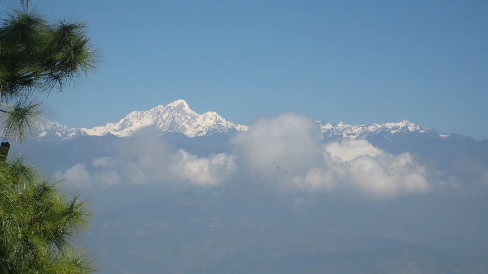 Layered green Himalayan foothills under a clear sky seen from Nagarkot ridge in Nepal, with distant snow peaks on the horizon.